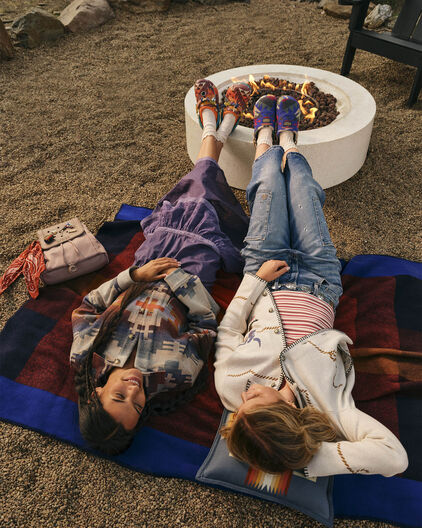 Two women outside by a fire pit wearing Crocs x Pendleton clogs