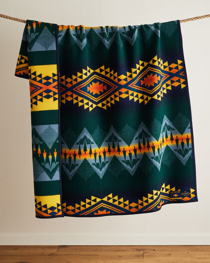 Wild Land Heroes blanket with dark blue orange and yellow patten, draped in front of a cream wall