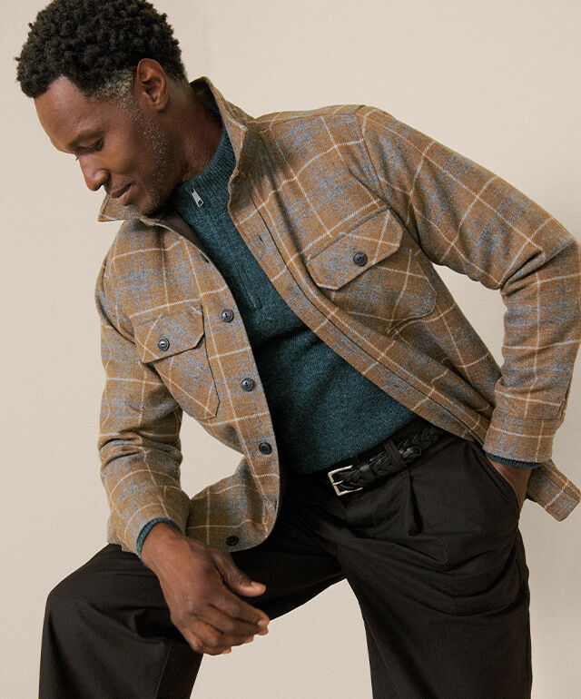 Man indoors wearing Pendleton plaid button up shit, standing with arm resting on knee