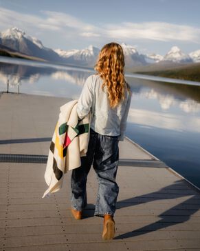 Woman walking on lake dock in Glacier National Park carrying a Pendleton blanket