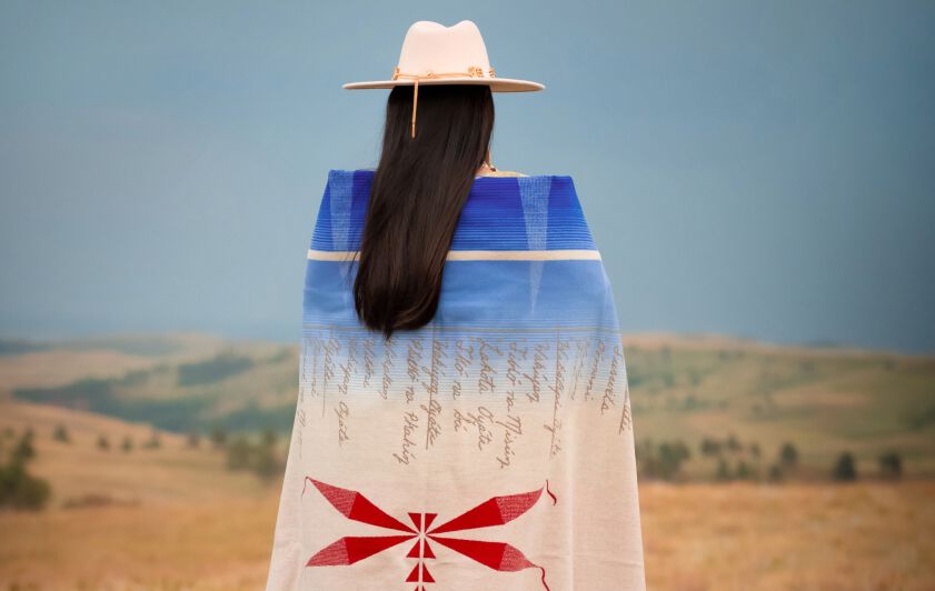 Artist Belle Brings Plenty standing wrapped in her Journey blanket