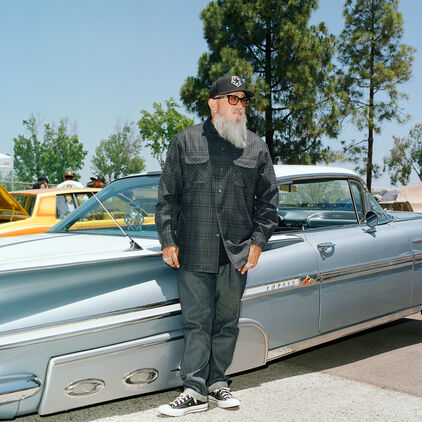 Artist Bobby Ruiz standing in front of vintage cars